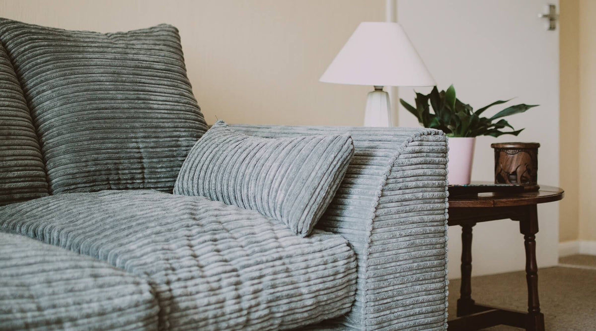 A close-up of a textured gray corduroy sofa with a matching throw pillow, next to a wooden side table