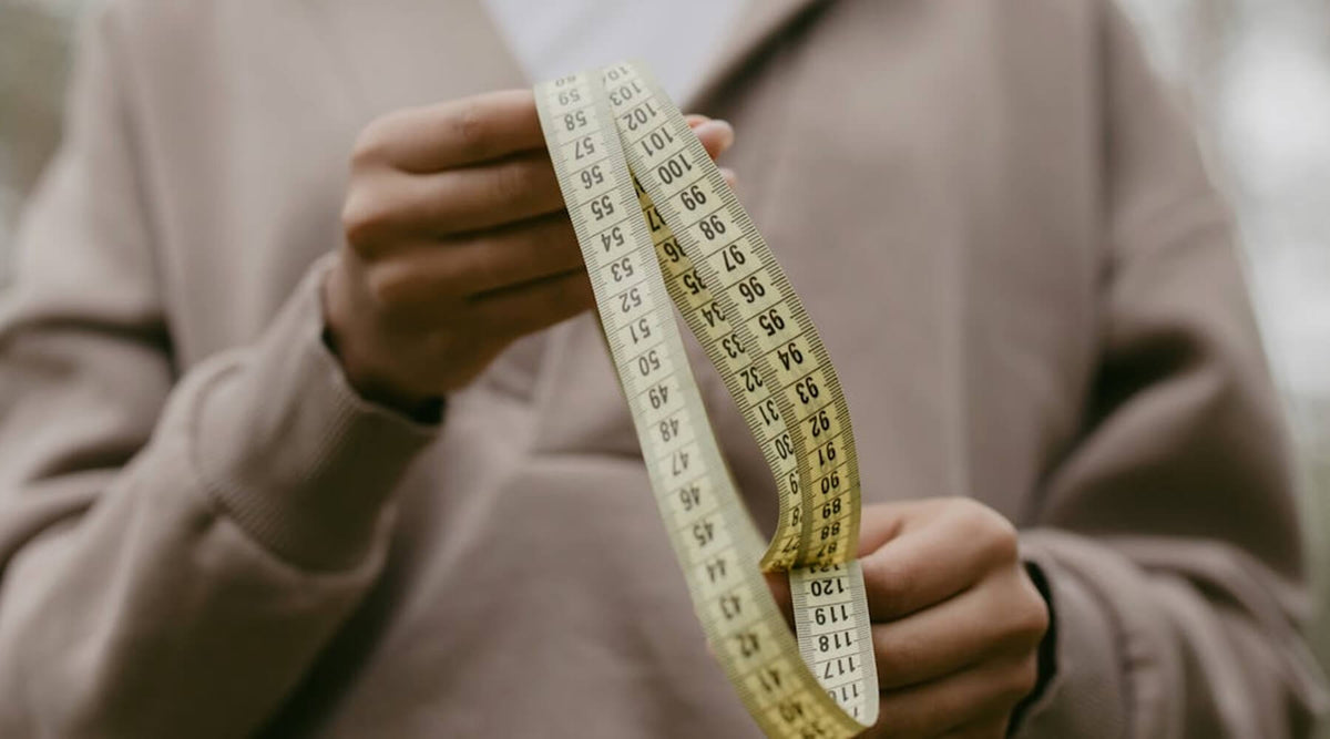 A person holds a measuring tape, demonstrating how to determine if a Cat-e-Corner scratcher will fit a sofa with the availability of a 3D mockup