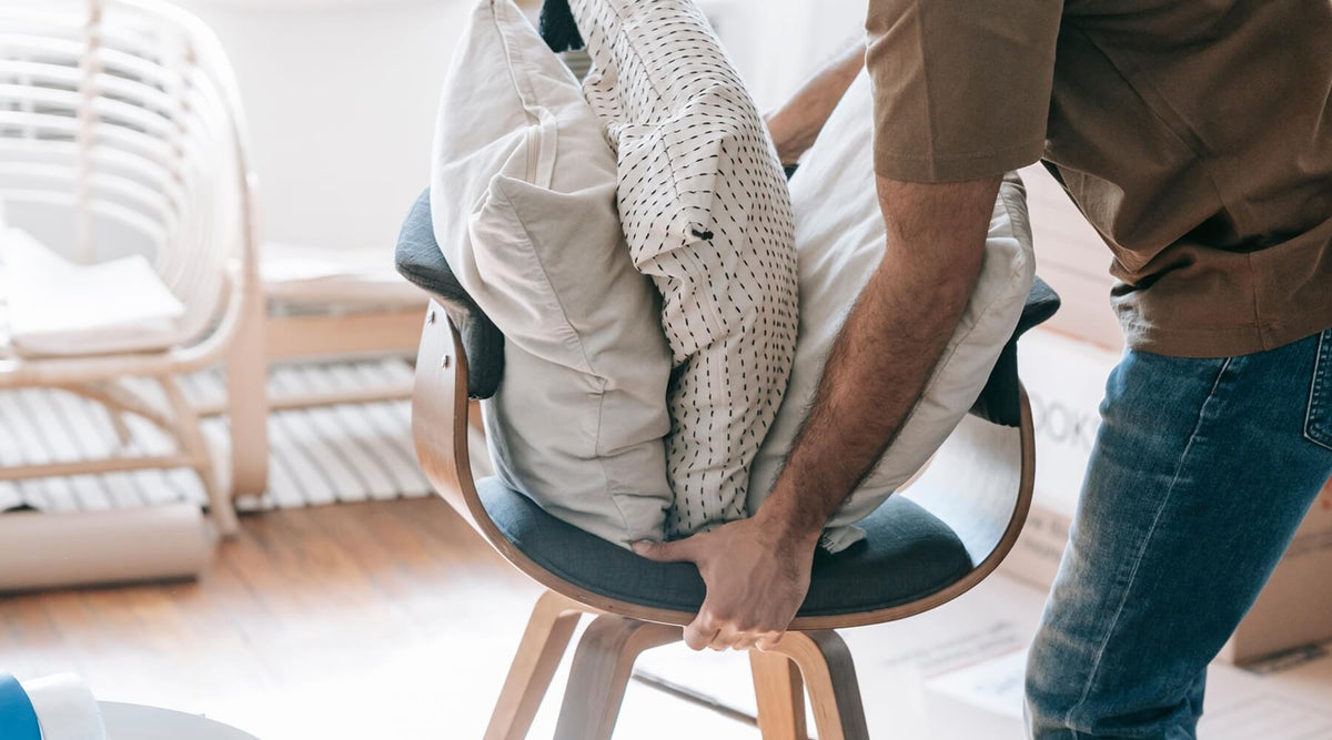 A person moves a chair laden with pillows and clothes, illustrating the potential for cat scratching after rearranging room