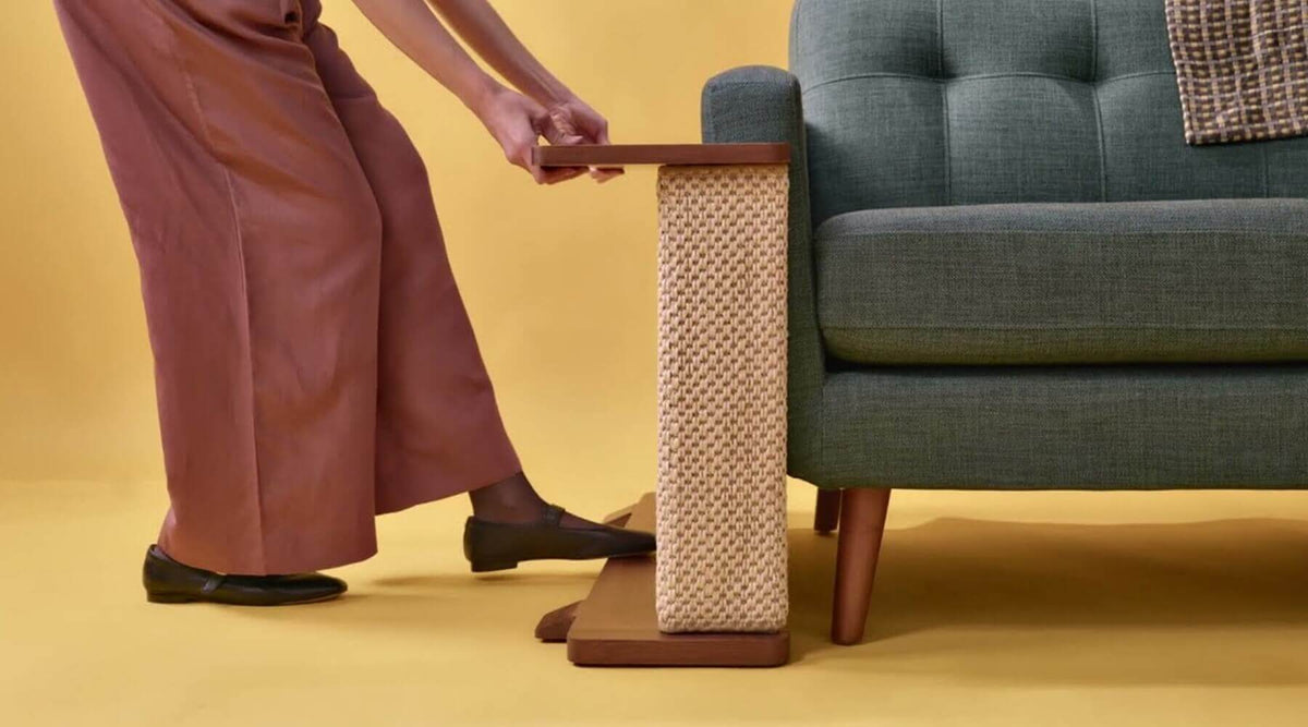 A person placing a sisal scratcher against a sofa arm, a perfect solution for cat-proofing a rental and protecting furniture you don't own