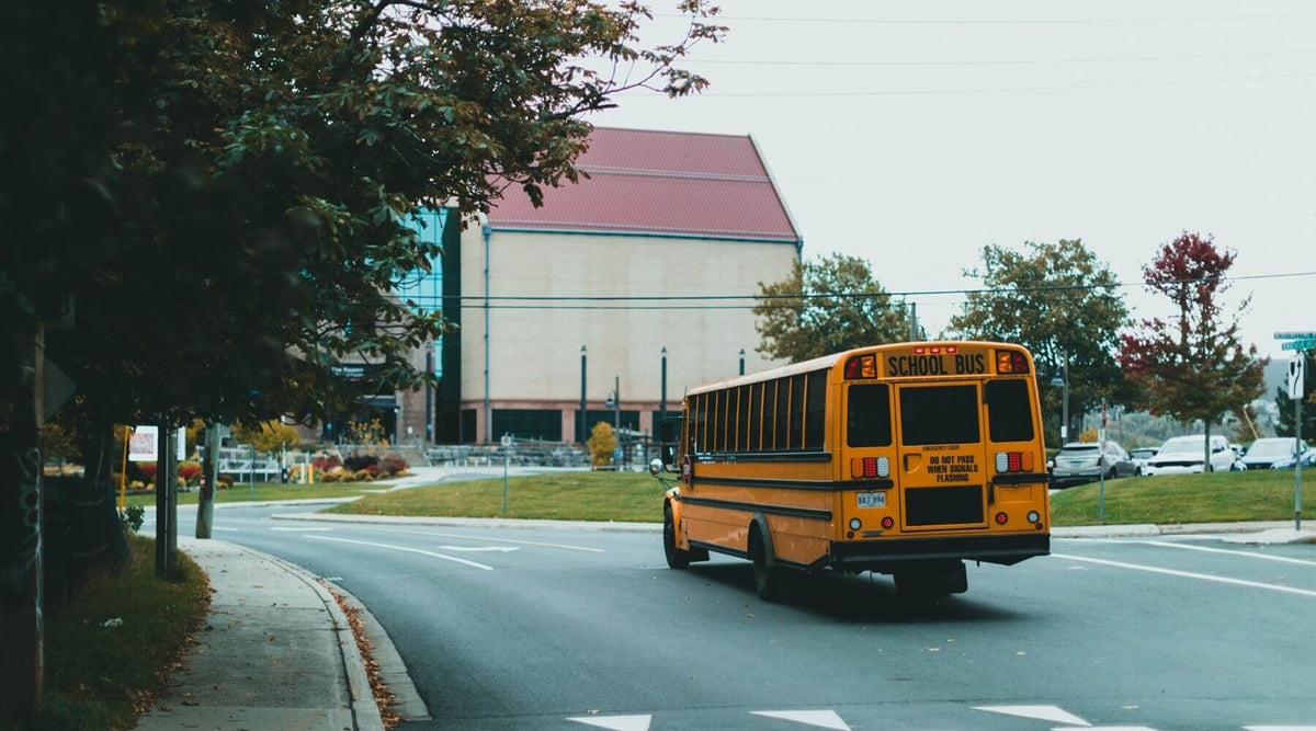 A yellow school bus driving away down a street
