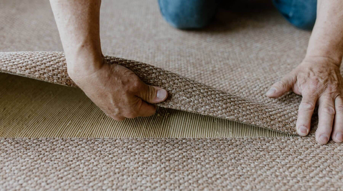 Hands installing a textured rug, showcasing sisal rugs in homes with cats