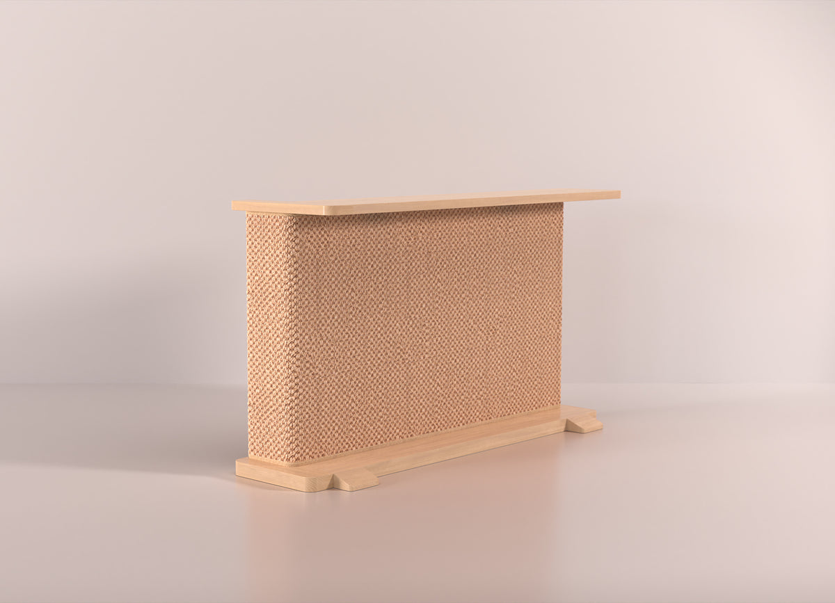 A Cat-e-Corner table placed next to a sofa, integrating a cat's scratching post with a small table, in a room with a plant and a colorful cushion.